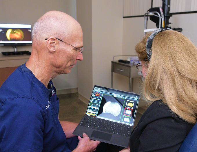 Eye care provider showing a patient retinal scan images on a laptop during an ophthalmology visit.