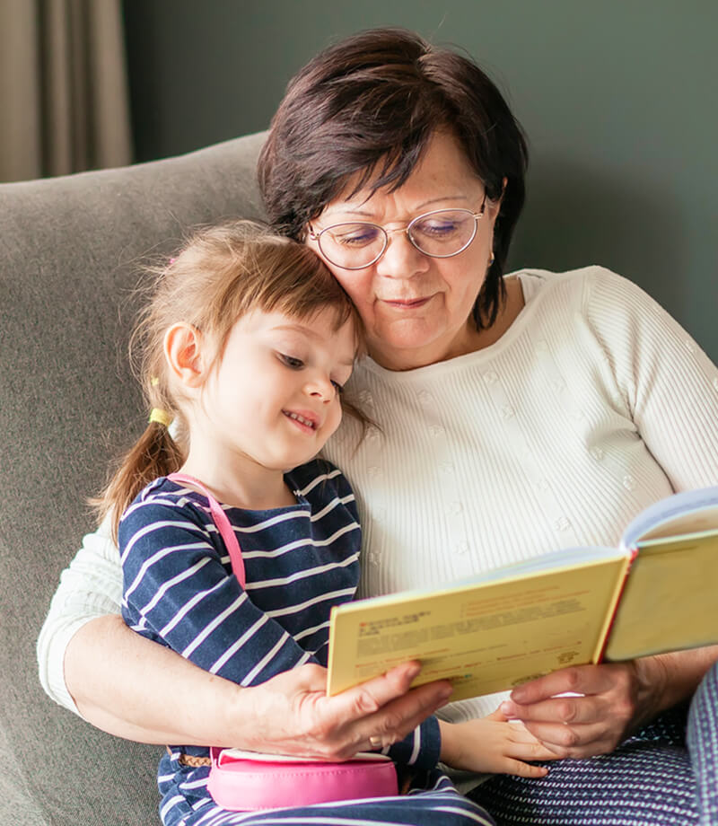 Grandmother reading a children&rsquo;s book with her granddaughter at home.