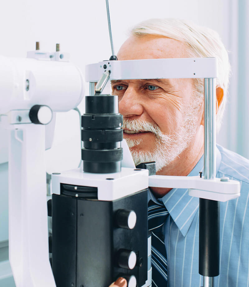 Older male patient looking into a slit lamp during a comprehensive eye examination.